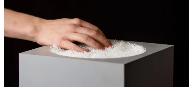 A hand hovers over a white fibrous surface on a dark rectangular base.